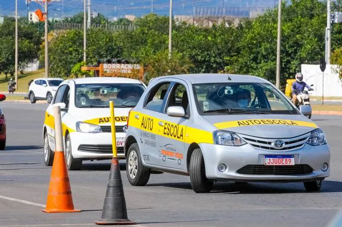 Carros de Autoescola em Treinamento com Veículos Automáticos. Dois carros de autoescola com faixas amarelas em circuito de treinamento, evidenciando a utilização de veículos automáticos durante o exame prático.
