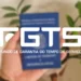 Carteira azul do FGTS sendo segurada por uma mão, representando o Fundo de Garantia do Tempo de Serviço no Brasil.