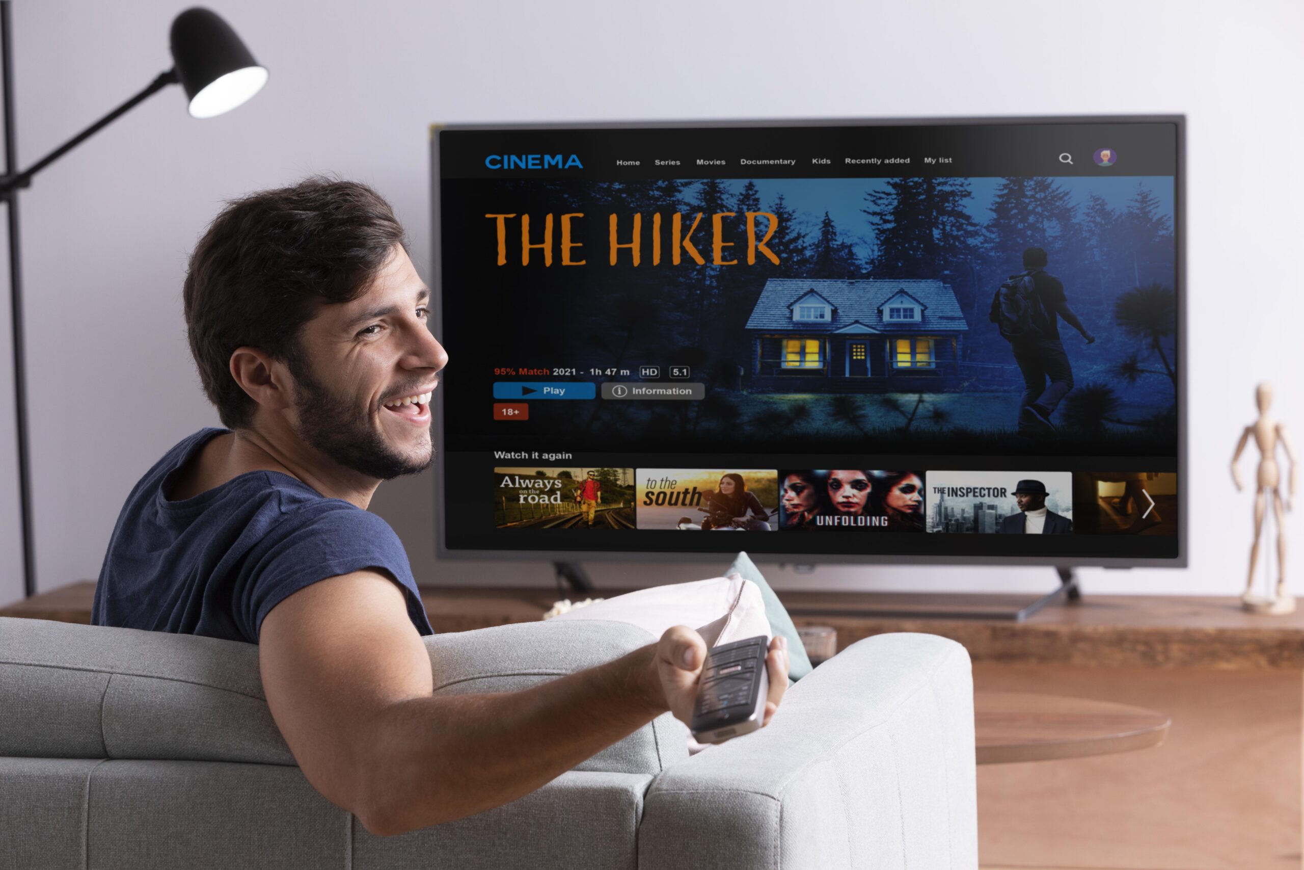 Homem assistindo filme The Hiker na TV Homem sorridente no sofá com controle remoto assistindo o filme The Hiker na televisão
