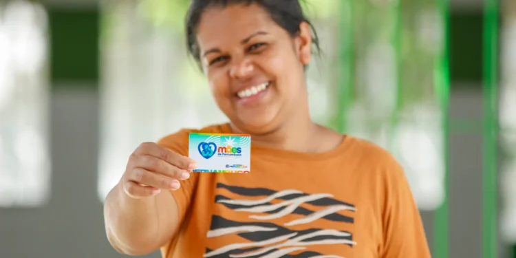 Mulher sorrindo enquanto segura um cartão do programa “Mães de Pernambuco”.