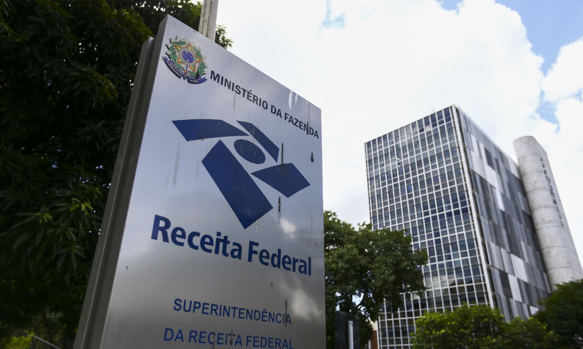 Receita Federal: Superintendência do Ministério da Fazenda em 2026. Placa da Receita Federal do Brasil ao lado de prédio moderno com árvores e céu azul, em 2026.