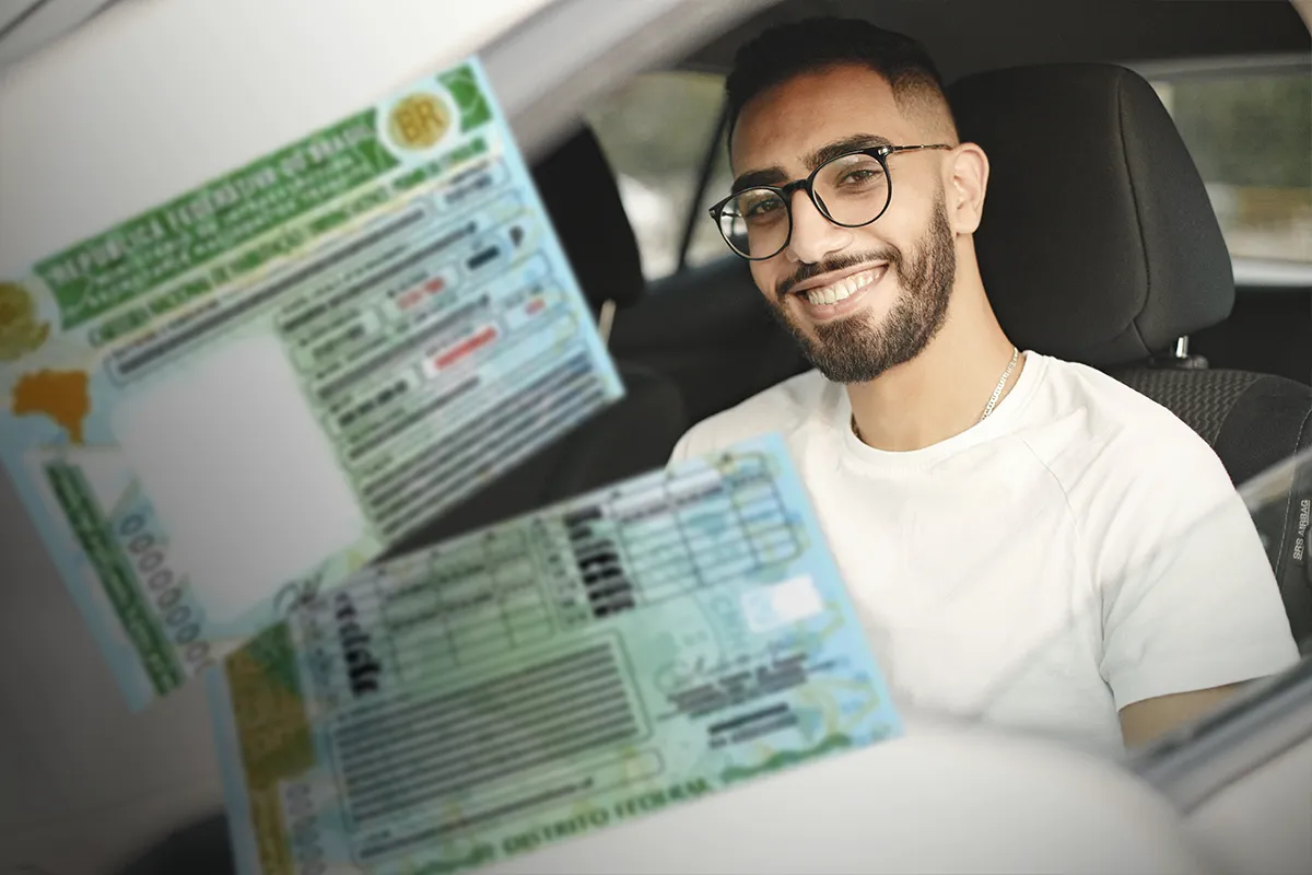 Homem sorridente com carteira de motorista brasileira Jovem homem sorridente dentro de carro segurando carteira de motorista do Brasil