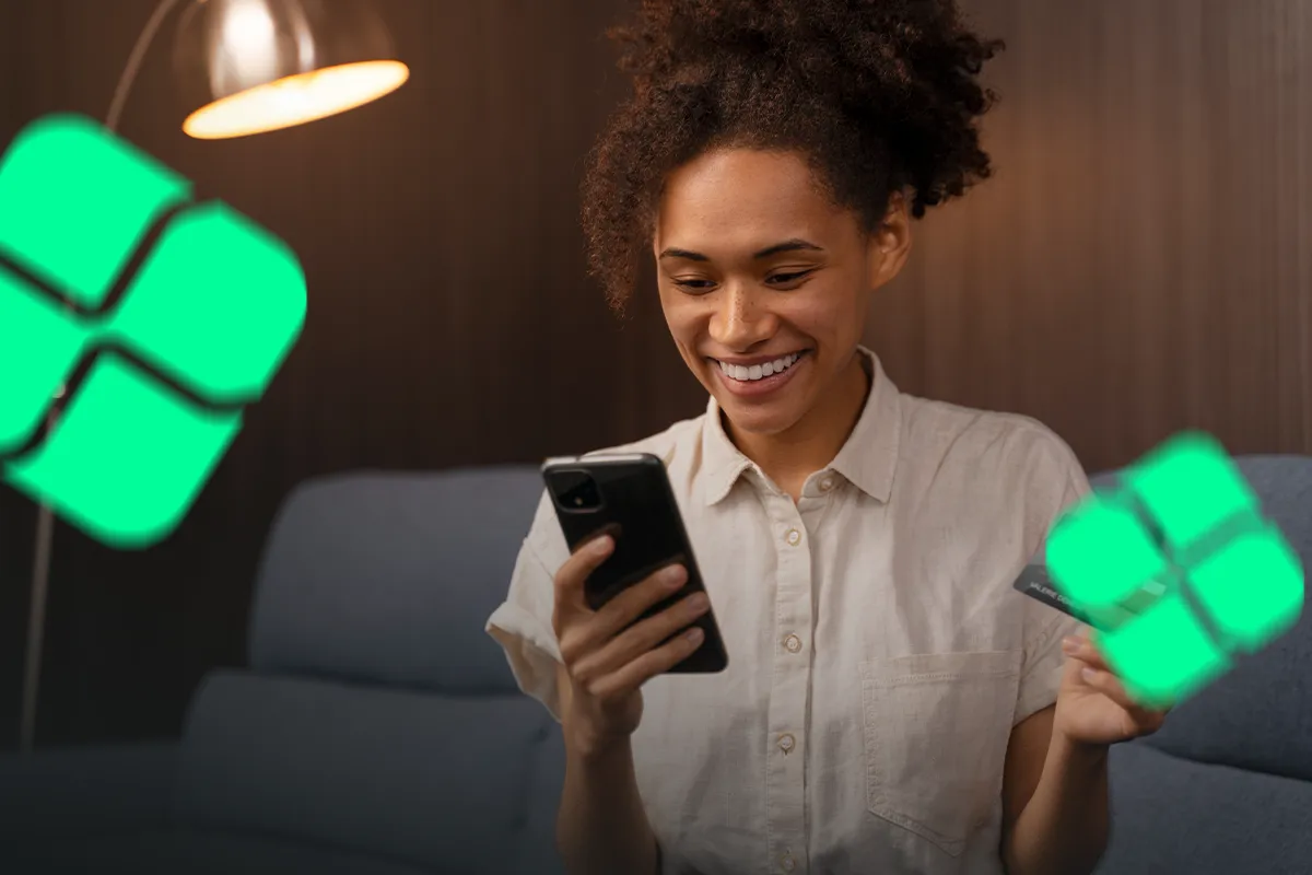 Jovem utilizando app bancário digital em ambiente doméstico Mulher sorridente usa smartphone segurando cartão enquanto senta em sofá iluminado