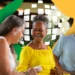 Três idosos sorrindo sentados juntos, com fundo colorido e ambiente externo