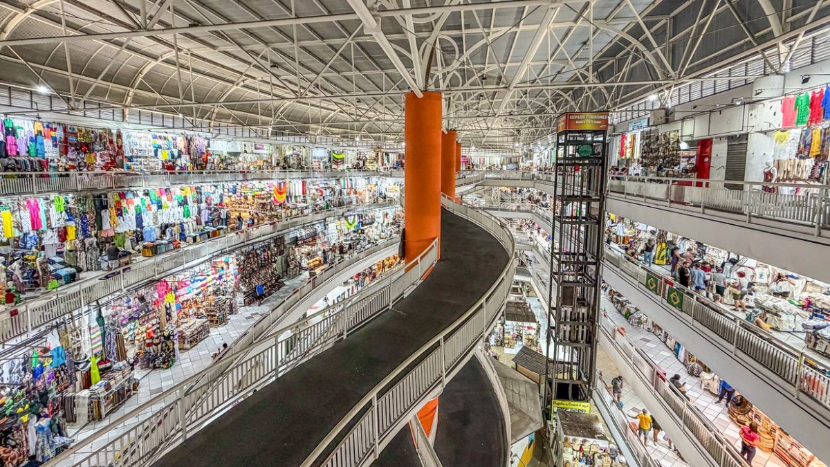 Vista interna de um grande mercado popular de vários pavimentos, com lojas de roupas e artigos variados, retratando o comércio varejista que passa a seguir a nova regra de trabalho em feriados.