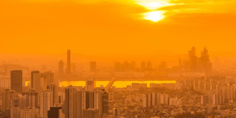 Prédios altos de cidade grande banhados por intensa luz alaranjada do pôr do sol em dia de calor extremo.