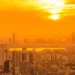 Prédios altos de cidade grande banhados por intensa luz alaranjada do pôr do sol em dia de calor extremo.