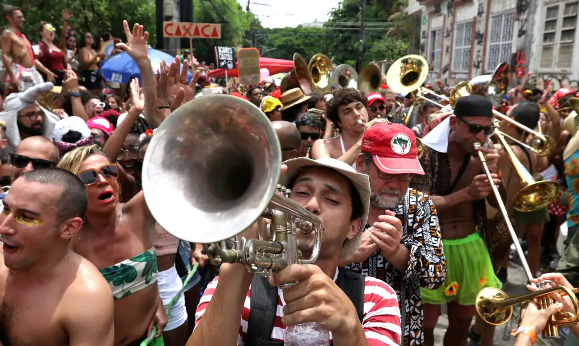 Bloco de rua anima foliões no carnaval brasileiro 2026 Músico toca trompete em meio a multidão de foliões fantasiados durante bloco de carnaval