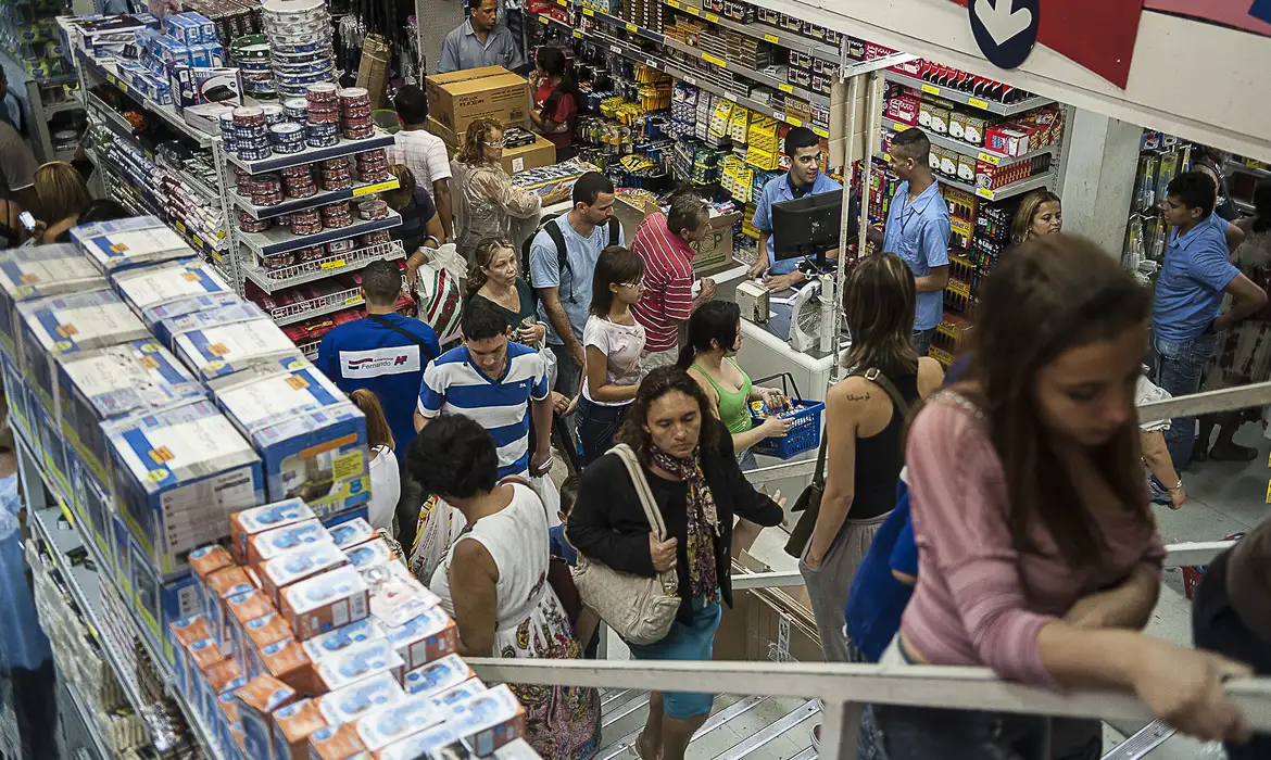 Consumidores fazem compras em supermercado lotado no início de 2026 Pessoas circulam e formam filas entre gôndolas de um supermercado repleto de produtos