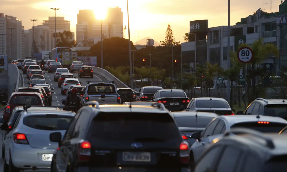 Trânsito intenso ao entardecer destaca importância do Curso teórico gratuito. Carros parados em congestionamento sob luz do pôr do sol em via urbana.