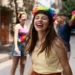 Mulher sorrindo com tiara de flores coloridas, amigos fantasiados em segundo plano na rua.
