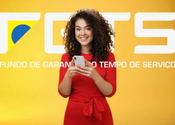 Mulher sorridente de vestido vermelho usa smartphone com logo do FGTS ao fundo amarelo.