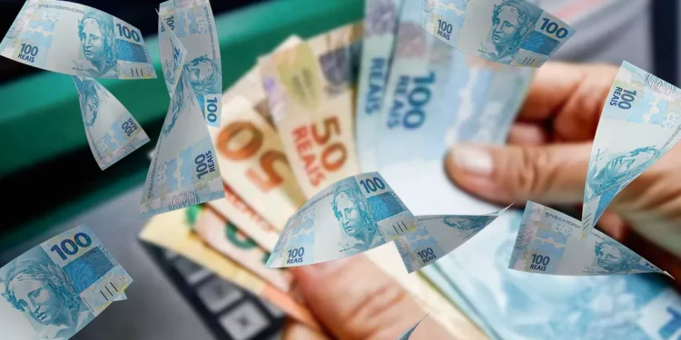 Mãos segurando notas de R$ 100 e R$ 50 em frente a caixa eletrônico, com dinheiro ao redor.