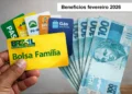 Mão segura cartões de benefícios sociais ao lado de cédulas de 100 reais.