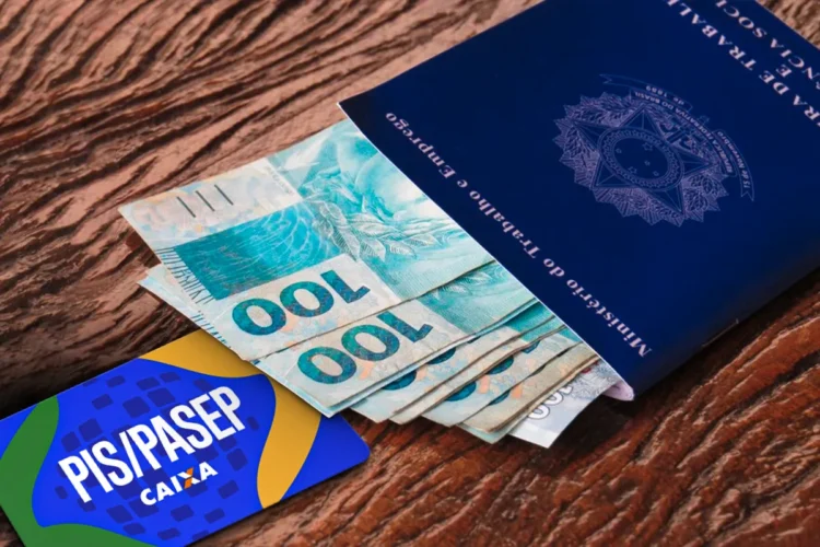 PIS/Pasep 2026 Carteira de trabalho com notas de R$ 100 e cartão PIS/PASEP sobre mesa de madeira