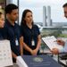 Três funcionários de loja, de camisa polo e crachá, observam um gestor apontar para uma planilha de escala de trabalho, ao lado de um calendário, da CLT e de um documento do Ministério do Trabalho, com o Congresso Nacional ao fundo, cenário da nova regra para o trabalho no comércio em feriados.