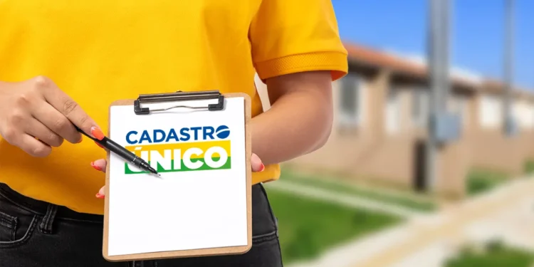 Mulher com camisa amarela aponta para prancheta com logo do Cadastro Único em área residencial.