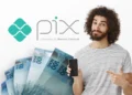 Homem sorrindo aponta para celular ao lado de notas de R$ 100 e logotipo do Pix.