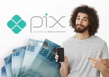 Homem sorrindo aponta para celular ao lado de notas de R$ 100 e logotipo do Pix.