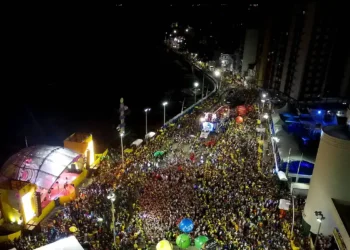 Pessoas fantasiadas lotam avenida iluminada durante desfile de bloco carnavalesco