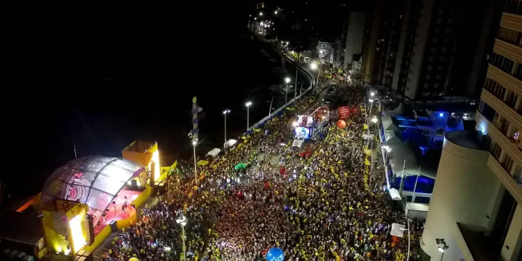 Pessoas fantasiadas lotam avenida iluminada durante desfile de bloco carnavalesco