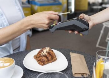 Pessoa aproxima cartão de máquina de pagamento ao comprar café e croissant em cafeteria