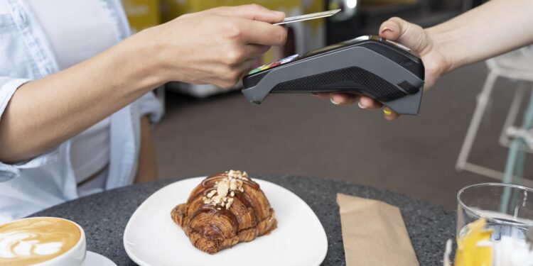 Pessoa aproxima cartão de máquina de pagamento ao comprar café e croissant em cafeteria