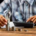 Pessoa empilhando moedas e segurando lâmpada ao lado de calculadora sobre mesa de madeira