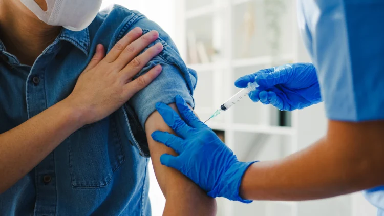 Profissional de saúde aplica vacina no braço de pessoa usando máscara