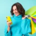 Mulher sorrindo segura várias sacolas de compras coloridas enquanto usa um celular amarelo