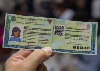 Mão segura nova Carteira de Identidade Nacional aberta com dados protegidos e QR Code visível