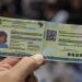 Mão segura nova Carteira de Identidade Nacional aberta com dados protegidos e QR Code visível