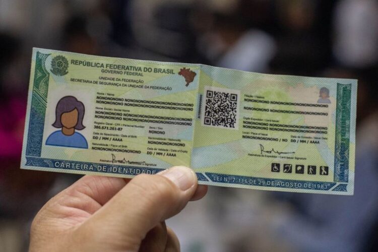 Mão segura carteira de identidade em novo formato, com QR Code visível e fundo desfocado