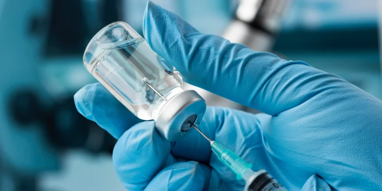 Mãos com luvas azuis seguram seringa extraindo líquido de frasco transparente