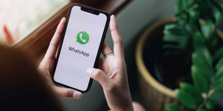 Mãos segurando um celular com o nome "WhatsApp" na tela.