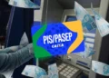Mãos segurando cartão PIS/PASEP da Caixa diante de caixa eletrônico com notas de R$ 100,00 ao redor.