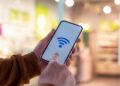 Mãos segurando smartphone com ícone de Wi-Fi azul na tela.