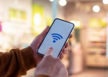 Mãos segurando smartphone com ícone de Wi-Fi azul na tela.