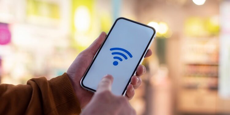 Mãos segurando smartphone com ícone de Wi-Fi azul na tela.