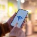 Mãos segurando smartphone com ícone de Wi-Fi azul na tela.