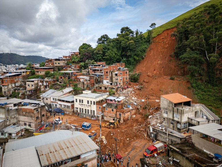 Vista aérea de deslizamento de terra em encosta, casas destruídas, equipes de resgate e veículo de bombeiros em Petrópolis.