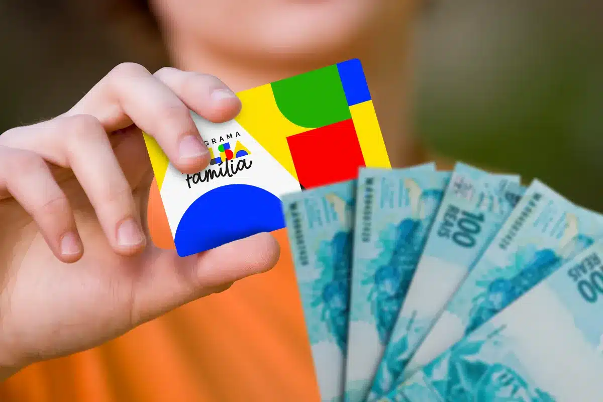 Mão segura cartão do Programa Bolsa Família ao lado de notas de cem reais, representando o acesso antecipado ao benefício por famílias de municípios em situação de emergência em abril de 2026.