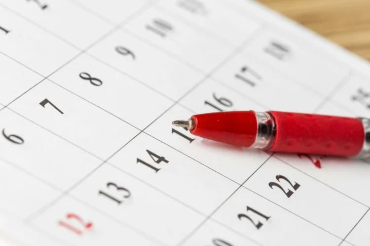 Caneta esferográfica vermelha sobre calendário mensal branco com números em preto, destacando os dias.