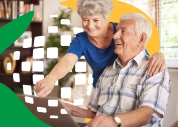 Casal de idosos sorrindo usando notebook em casa consultando benefício do INSS