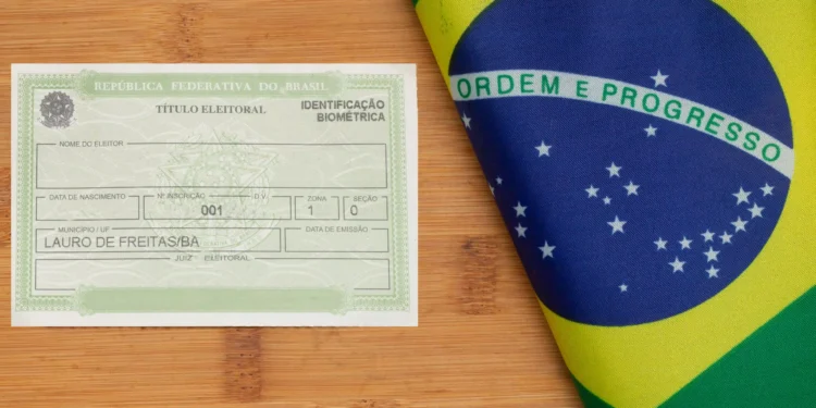 Título eleitoral da República Federativa do Brasil sobre mesa de madeira ao lado de bandeira nacional dobrada.