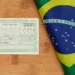 Título eleitoral da República Federativa do Brasil sobre mesa de madeira ao lado de bandeira nacional dobrada.