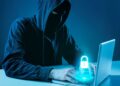 Ilustração de um hacker usando capuz e máscara escura em frente a um notebook em ambiente azulado. Sobre o teclado, há um holograma brilhante de um cadeado azul, simbolizando segurança digital e invasão de contas.