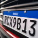 Placa Mercosul com fundo branco, faixa azul com "BRASIL" e bandeira, código RCX9B13 em caracteres pretos.