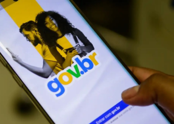 Mão segurando smartphone exibindo tela inicial do app Gov.br com casal sorrindo e logo colorido.
