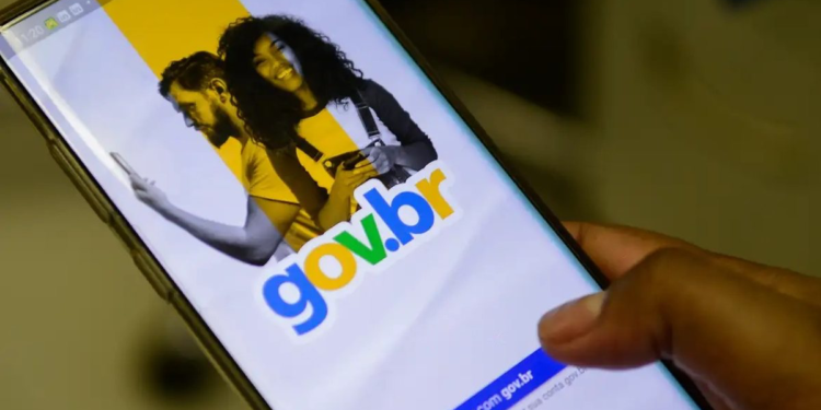 Mão segurando smartphone exibindo tela inicial do app Gov.br com casal sorrindo e logo colorido.